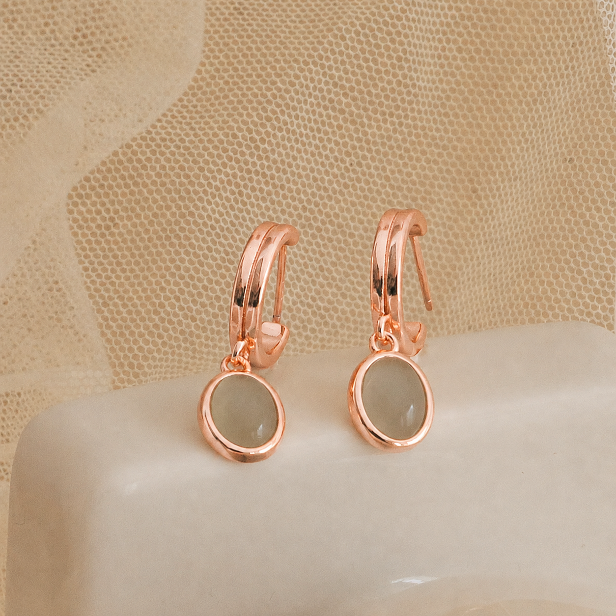Rose gold earrings with green gemstones on a beige surface